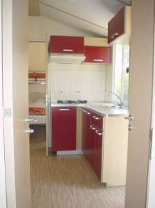 Una cucina compatta con mobili rossi e beige, piano cottura e lavello, in un piccolo spazio.