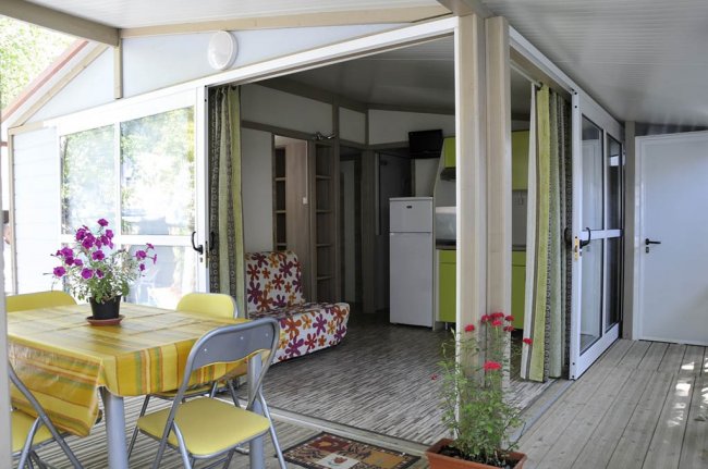 Patio con tavolo giallo, cucina aperta e piante fiorite.