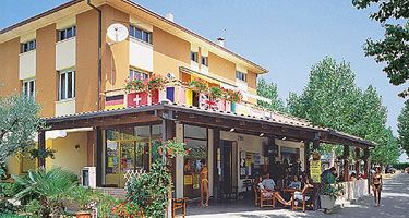 Un edificio giallo con veranda, bandiere appese e persone sedute all'esterno.