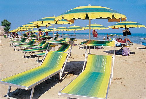 Una spiaggia con lettini verdi e gialli, sotto ombrelloni dello stesso colore, vicino al mare.