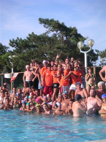 Grande gruppo di persone festanti in piscina, alcune in divise arancioni.