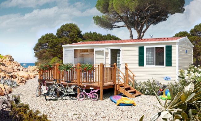 Casa mobile con veranda e biciclette, circondata da alberi.