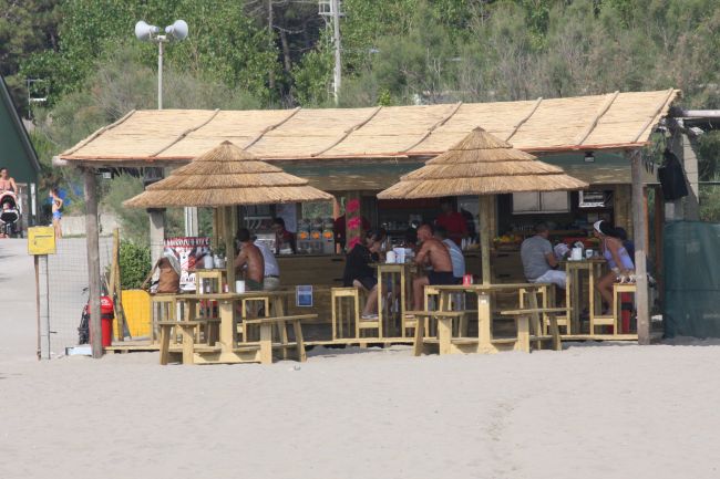 Chiosco in spiaggia con tetto di paglia e tavolini all'aperto.