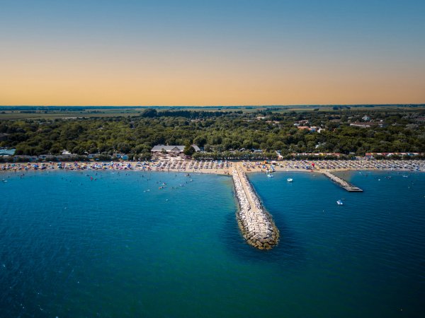 Spiaggia con pontile roccioso che si estende nel mare.