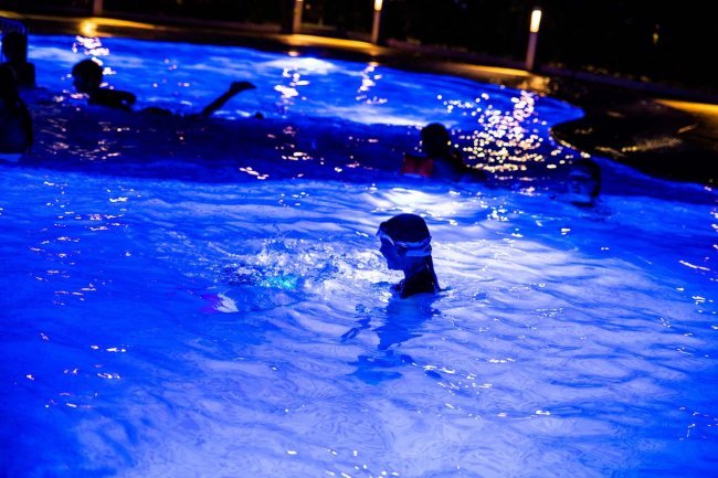 Bambino in una piscina illuminata di notte.