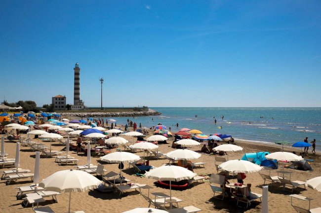 Spiaggia affollata con ombrelloni e faro.