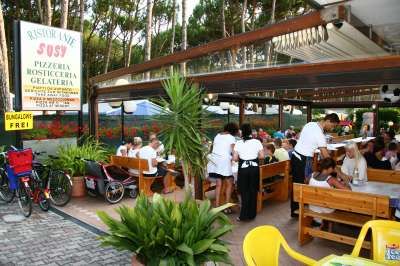 Ristorante all'aperto con tavoli di legno, persone sedute e personale in servizio.