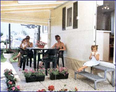 Persone sedute a un tavolo all'aperto vicino a un camper, con fiori intorno.